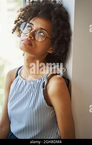 Femme attirante et attentionnés dans des lunettes circulaires placées près de la fenêtre Banque D'Images