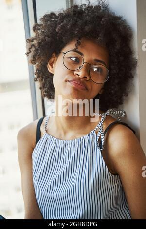 Jolie femme calme dans le cercle de lunettes assis près de la fenêtre Banque D'Images