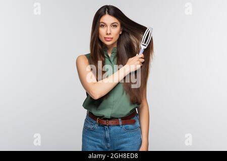 jolie jeune femme se brossant les cheveux longs isolés sur le gris Banque D'Images