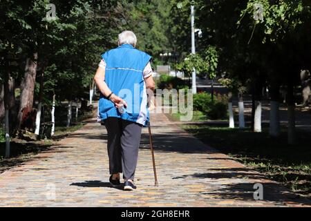 Vieille femme marchant avec une canne dans une rue du parc de la ville. La personne qui s'agine, les maladies de la colonne vertébrale, les personnes âgées Banque D'Images