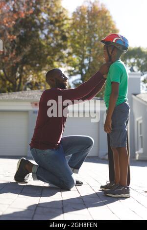 Père afro-américain avec son fils souriant et se préparant avant le skateboard dans le jardin Banque D'Images