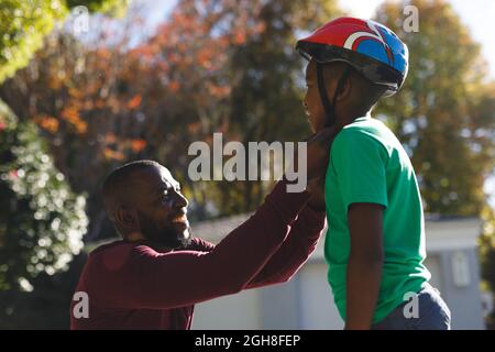 Père afro-américain avec son fils souriant et se préparant avant le skateboard dans le jardin Banque D'Images