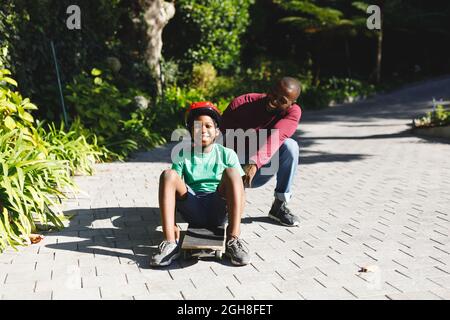 Portrait du père afro-américain avec son fils souriant et jouant avec le skateboard dans le jardin Banque D'Images