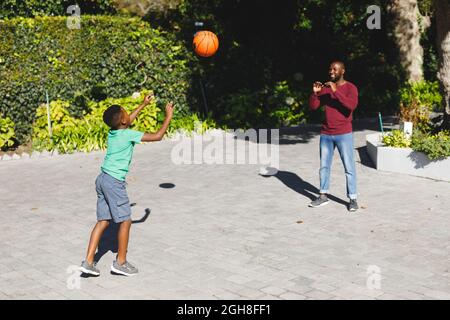 Père afro-américain avec son fils souriant et jouant au basket-ball dans le jardin Banque D'Images