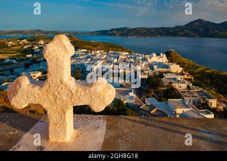 Croix chrétienne et village de Plaka sur l'île de Milos sur rouge Géranium fleurs au coucher du soleil en Grèce Banque D'Images