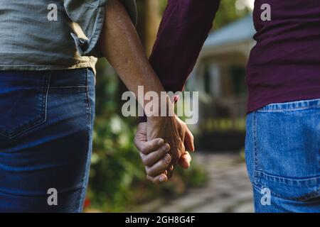 Section médiane d'un couple caucasien âgé tenant les mains marchant dans le jardin Banque D'Images