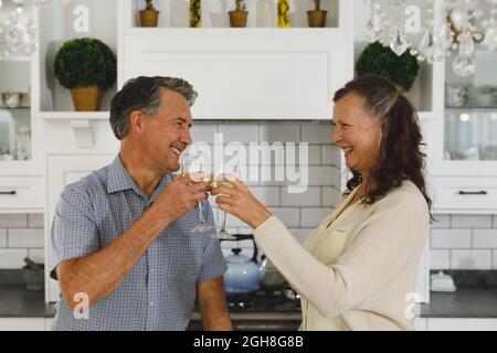 Joyeux couple caucasien âgé dans la cuisine moderne, boire du vin, faire un toast et sourire Banque D'Images