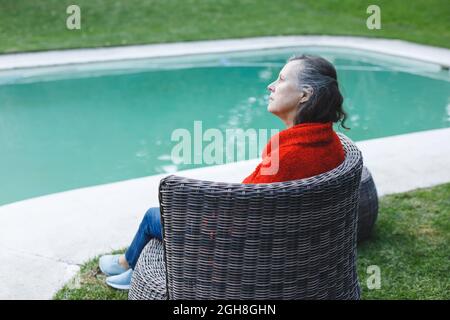 Femme de race blanche, très attentionnés, assise sur une chaise près de la piscine dans le jardin Banque D'Images