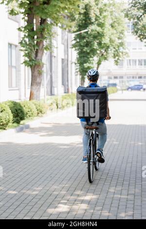 Vue arrière du coursier avec sac à dos thermo à vélo dans la rue urbaine Banque D'Images