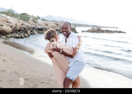 Couple souriant de race mixte appréciant sur les vacances, touriste ayant plaisir à marcher sur le bord de la plage, diversité et concept d'amour. Banque D'Images