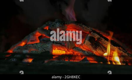 Gros plan du feu intérieur pour l'arrière-plan. Feu de camp barbecue la nuit. Faible luminosité avec mise au point sélective. Texture des flammes avec des charbons et du bois de chauffage Banque D'Images