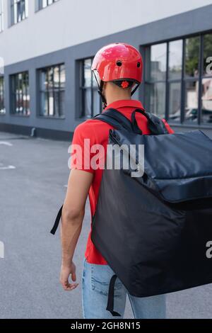 Vue arrière du messager dans un casque et un sac à dos thermo debout à l'extérieur Banque D'Images