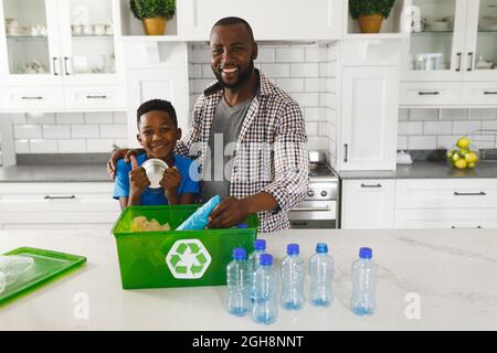 Portrait d'un heureux père et fils afro-américains dans la cuisine triant les ordures pour recyclage Banque D'Images