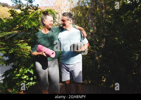 Joyeux couple caucasien expérimenté pratiquant le yoga, tenant des tapis de yoga dans le jardin ensoleillé Banque D'Images