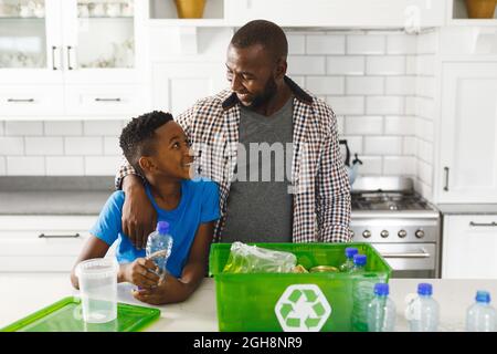 Joyeux père et fils afro-américains en cuisine parlant et triant des ordures pour recyclage Banque D'Images