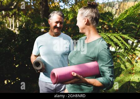 Joyeux couple caucasien expérimenté pratiquant le yoga, tenant des tapis de yoga dans le jardin ensoleillé Banque D'Images