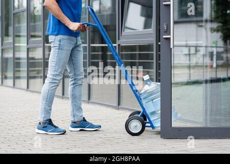 Vue rognée du chariot de transport de coursier avec une bouteille d'eau près de la porte ouverte du bâtiment Banque D'Images