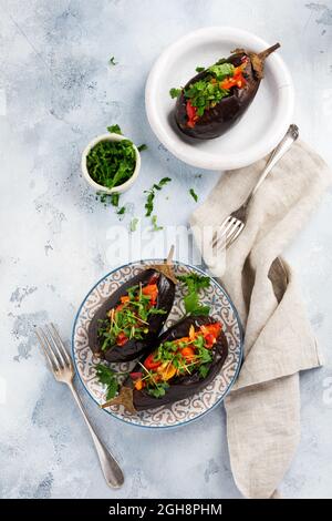 Aubergine farcie cuite avec différents légumes, tomate, poivre, oignon et persil sur fond de table en pierre grise ou en béton. Vue de dessus Banque D'Images