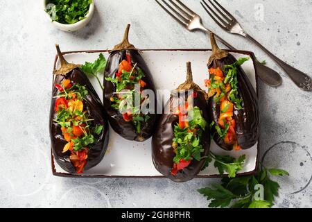 Aubergine farcie cuite avec différents légumes, tomate, poivre, oignon et persil sur fond de table en pierre grise ou en béton. Vue de dessus Banque D'Images