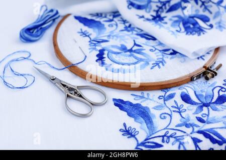 Cerceau à broderie avec tissu, aiguille et fil à coudre. Motif brodé fait main de fleurs bleues sur fond blanc Banque D'Images