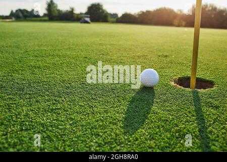 Balle de golf près du trou avec un drapeau sur le parcours de golf, journée ensoleillée, gros plan Banque D'Images