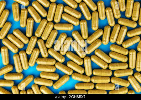 Capsules de pilules jaunes kaki sur fond de papier bleu. Concept médicinal plein cadre. Vue de dessus. Pose à plat Banque D'Images