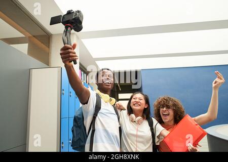 Groupe d'élèves souriants blogging à l'école. Groupe multiethnique de jeunes enregistrant une vidéo avec une caméra professionnelle. Banque D'Images