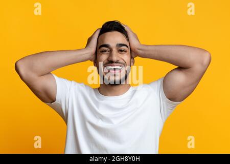 Super heureux moyen-oriental gars souriant et touchant sa tête Banque D'Images