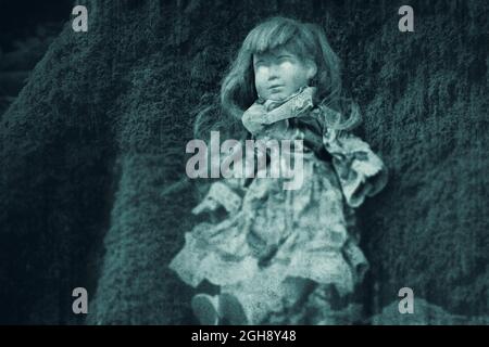 Un concept d'horreur d'une poupée possédée, avec des yeux brillants. Assis dans une forêt. Avec un montage grunge et vintage. Banque D'Images