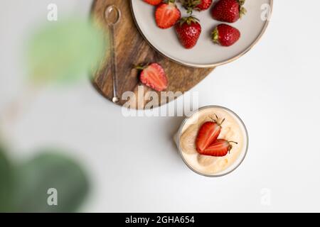 Cheesecakes à la fraise avec des fraises fraîches dans un plat avec un délicat dessert tiramisu sur une table en bois blanc, espace pour les copies, vue du dessus Banque D'Images