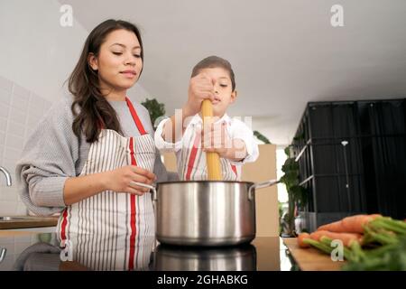 Dans la cuisine : une famille monoparentale cuisant des pâtes ensemble. Mère et fils mettant des pâtes à ébullition. Les enfants aident les parents. Une alimentation saine. Banque D'Images