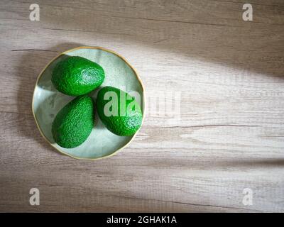 trois avocats verts sur plaque sur surface en bois Banque D'Images