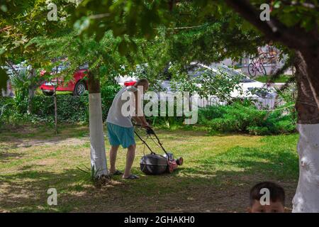 Vieux grand-père fauchant la pelouse. Joyeux homme âgé qui travaille Banque D'Images