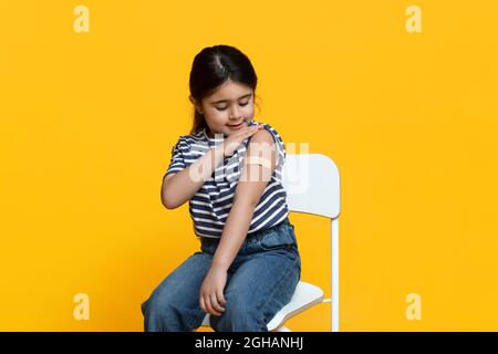 Vaccination Covid-19. Petite fille vaccinée regardant bras avec plâtre après injection Banque D'Images