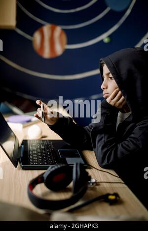 Garçon tenant un disque de violon regardant un ordinateur portable dans la chambre Banque D'Images