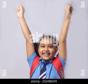 Une heureuse jeune fille indienne souriante étudiante en uniforme d'école bleu avec sac rouge sur fond gris Banque D'Images