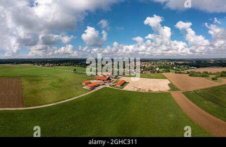 Vue aérienne sur un ranch avec des chevaux et un village à l'arrière-plan sous un ciel bleu et moelleux et nuageux. Banque D'Images