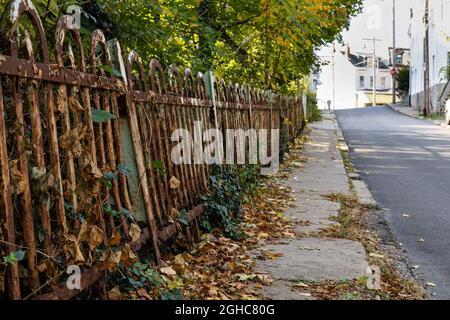 Vue basse sur un long trottoir étroit avec clôture en fer forgé rouillé, feuilles d'automne, aspect horizontal Banque D'Images