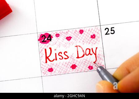 Une femme doigts avec un stylo écrire un rappel Kiss Day dans le calendrier. Septembre 24. Banque D'Images