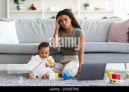 Mère noire stressée essayant de travailler à la maison pendant que bébé la distraire Banque D'Images