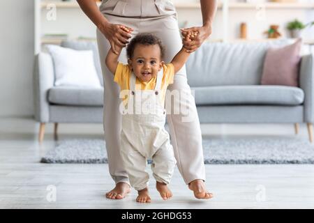 Adorable bébé noir fait les premiers pas à la maison avec l'aide de la mère Banque D'Images