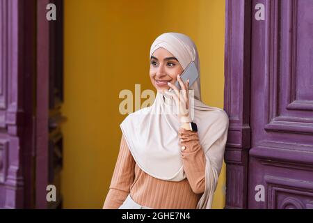 Bonne femme islamique millénaire dans hijab bonne journée et week-end, parler au téléphone Banque D'Images