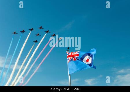 RAF Royal Air Force Red flèches avions à réaction survolant le drapeau de raf ensign. L'équipe d'exposition aérienne britannique flotte au-dessus du drapeau et de la cocarde Union Jack. Ciel bleu Banque D'Images