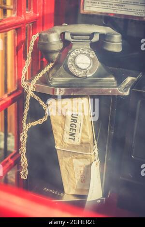 Vue à travers le verre d'une ancienne boîte téléphonique rouge britannique traditionnelle en regardant un colis urgent laissé sur la tablette sous le combiné vintage. Banque D'Images