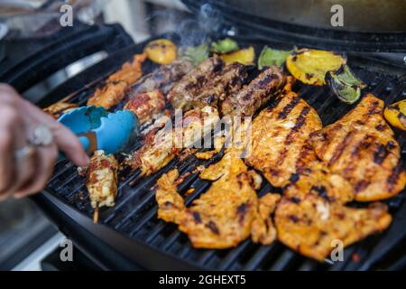 Une personne utilise des langues pour faire cuire du poulet et de l'agneau à l'extérieur sur un barbecue à Londres, en Angleterre. Banque D'Images