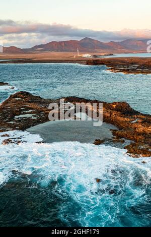 Vue aérienne des vagues de l'océan s'écrasant sur les rochers au coucher du soleil, Punta Jandia, Fuerteventura, îles Canaries, Espagne Banque D'Images