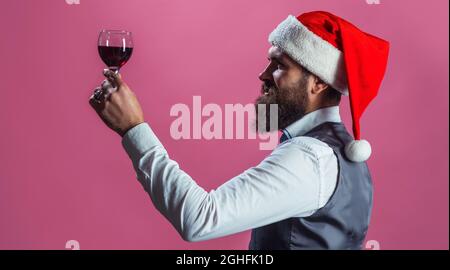 Santa avec un verre de vin rouge. Dégustation d'alcool. L'homme barbu au cap du Père Noël boit du vin. Fête du nouvel an. Banque D'Images