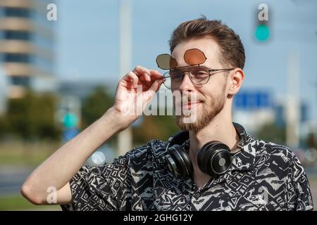 Portrait d'un jeune homme en lunettes de soleil et écouteurs sur le fond d'une ville moderne Banque D'Images