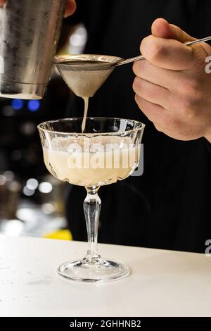 Le barman professionnel verse le cocktail alcoolisé orange du shaker au verre à l'aide d'un tamis. Flou Banque D'Images