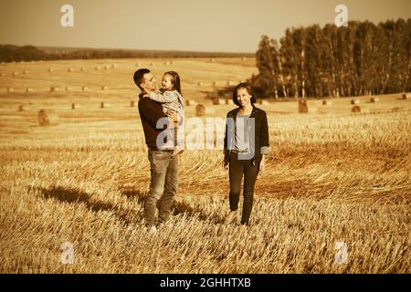 Bonne jeune famille avec bébé fille de deux ans marchant dans le champ de récolte Banque D'Images